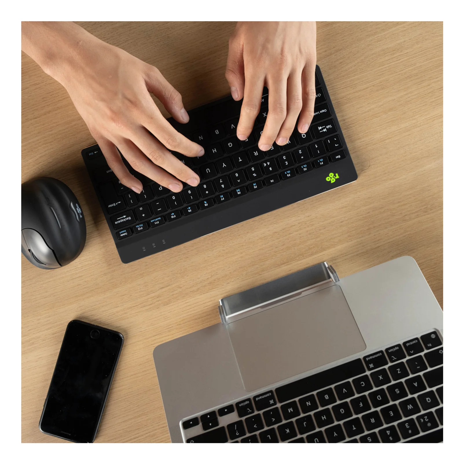 Mains tapant sur le clavier R-Go posé sur bureau bois, smartphone à gauche et laptop en arrière-plan