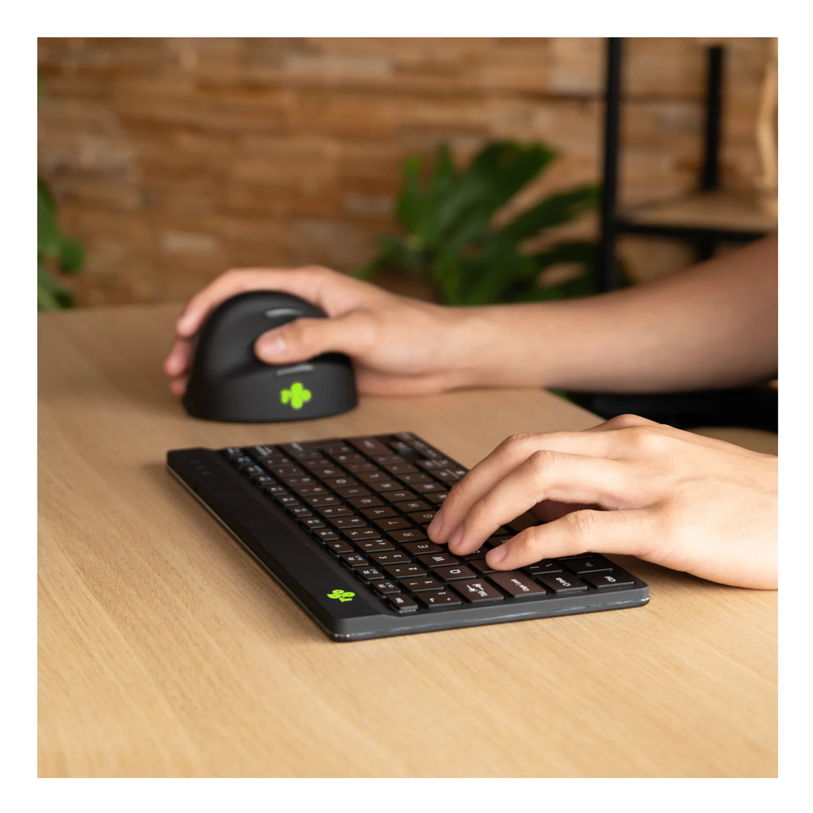 Main droite sur souris verticale noire, main gauche sur clavier R-Go compact, bureau bois
