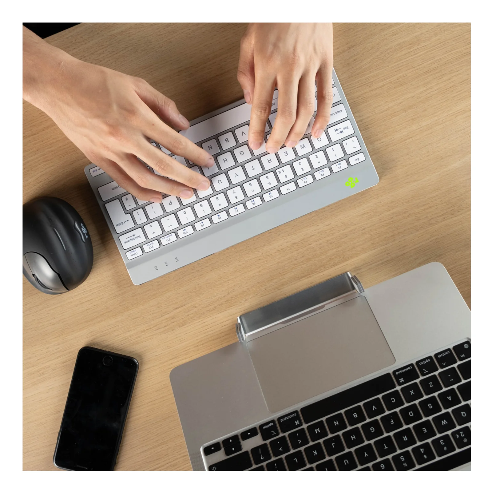 Mise en situation sur bureau bois, clavier blanc à côté d'un laptop argenté, souris noire et smartphone