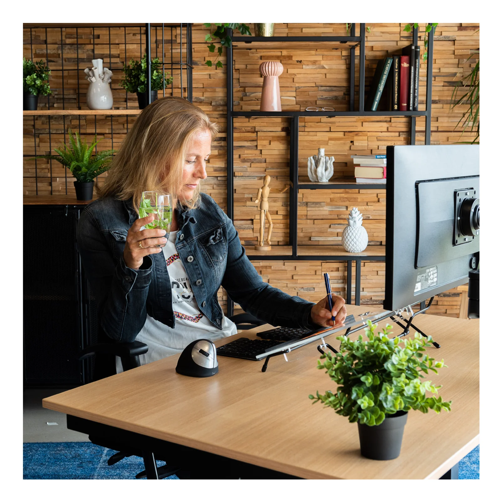 Femme travaillant au bureau avec porte-documents ergonomique, moniteur et plantes en arrière-plan