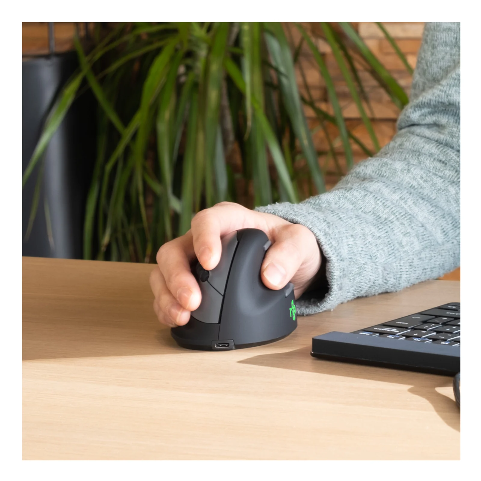 Main utilisant la souris R-Go HE Break sur bureau, clavier et plante visibles, LED verte allumée