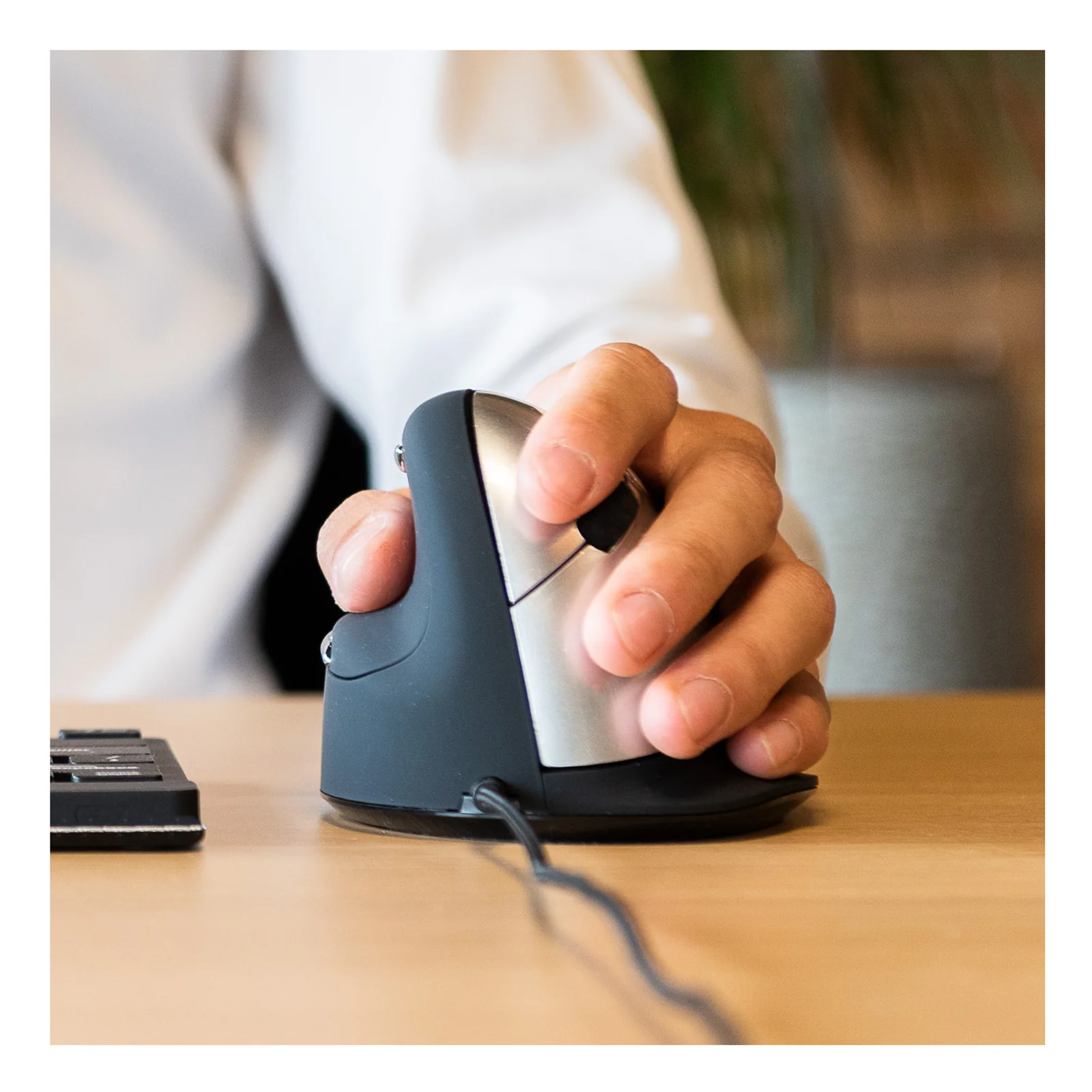 Main tenant la souris ergonomique verticale noire sur un bureau, vue de côté