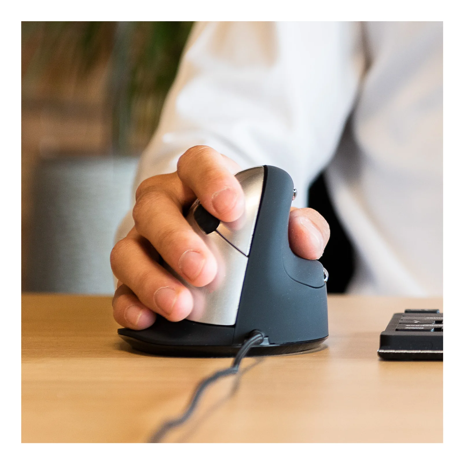 Personne tenant la souris verticale noire en position naturelle sur bureau en bois