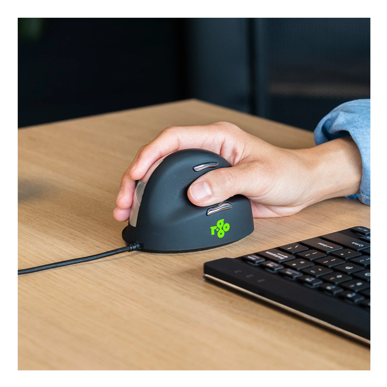 Main utilisant la souris HE Break noire sur un bureau, clavier visible en arrière-plan