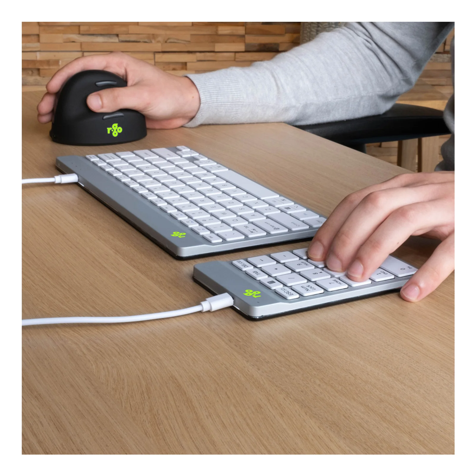 Main utilisant le pavé numérique blanc R-Go à côté d'un clavier compact et d'une souris ergonomique verticale noire sur bureau en bois
