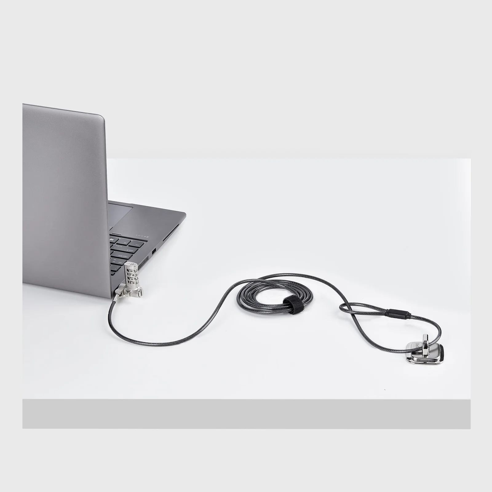 Câble antivol branché sur un ordinateur portable posé sur une surface blanche, extrémité libre avec adaptateur universel visible