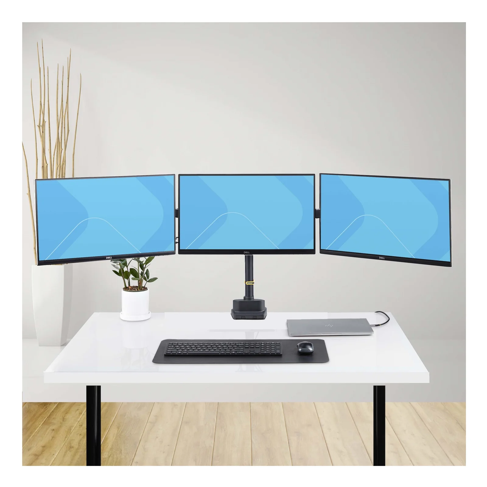 Vue d'ensemble lifestyle du support triple moniteur StarTech.com sur un bureau blanc dans un espace de travail ouvert, ordinateur portable posé à droite.