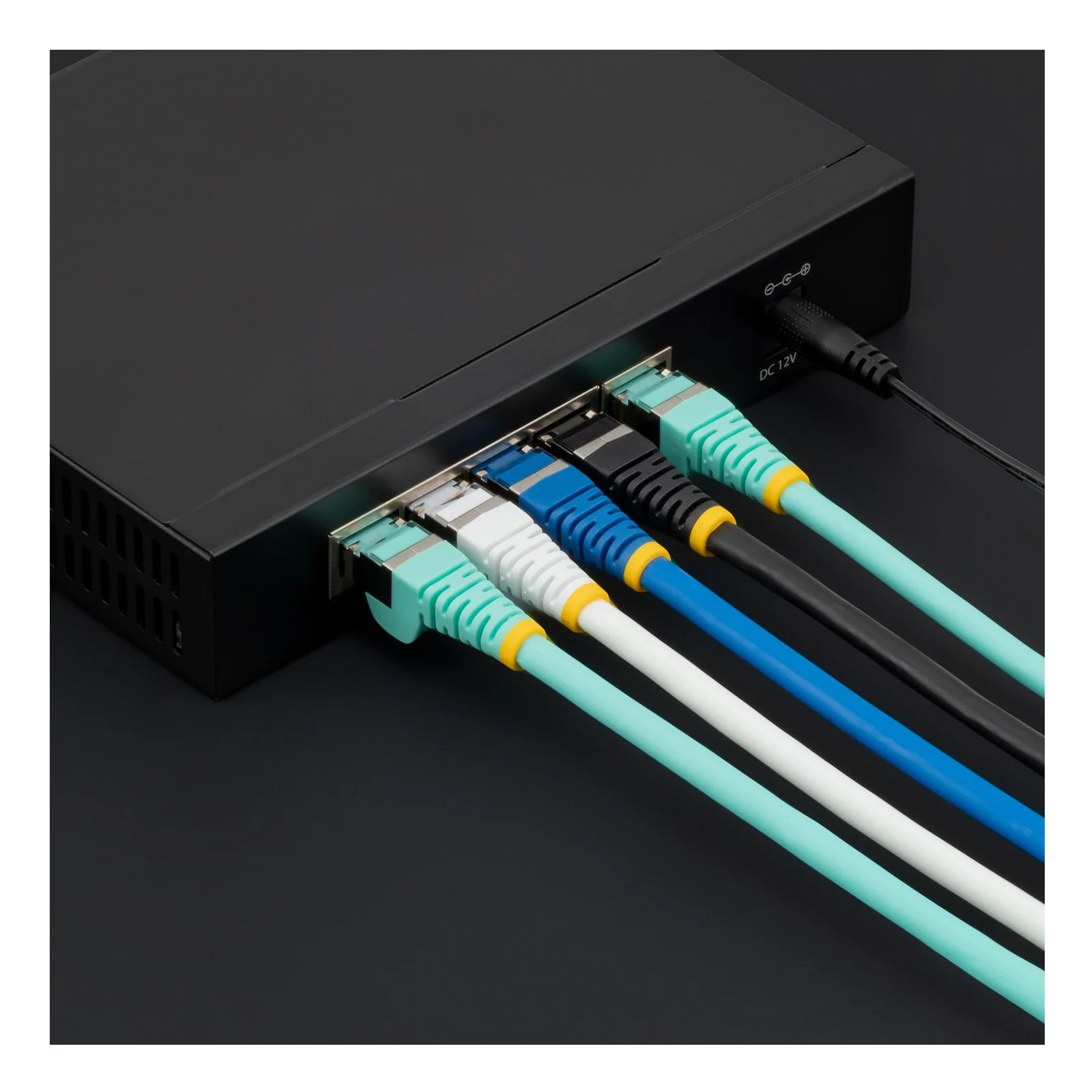 Cinq câbles réseau de couleurs différentes branchés sur les ports d'un switch réseau noir, dont un câble noir avec bague jaune