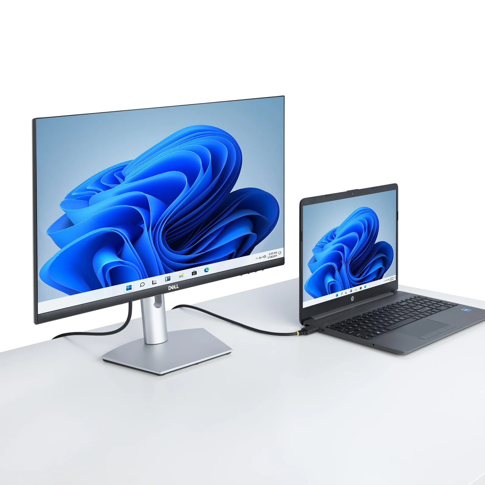 Câble HDMI noir connecté entre un moniteur et un ordinateur portable affichant tous deux un fond d'écran bleu, sur un bureau blanc