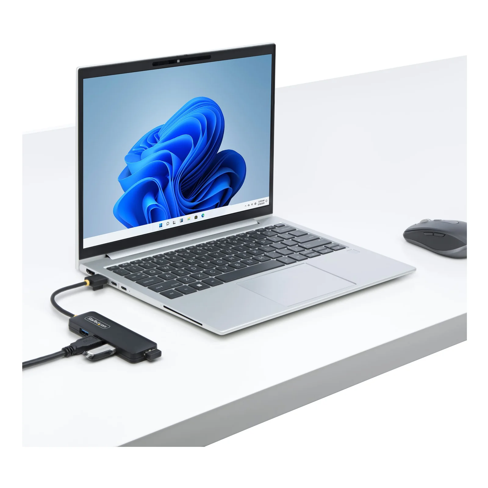 Hub USB-A 4 ports connecté à la tranche d'un ordinateur portable argenté sur un bureau blanc, plusieurs périphériques branchés sur les ports du hub