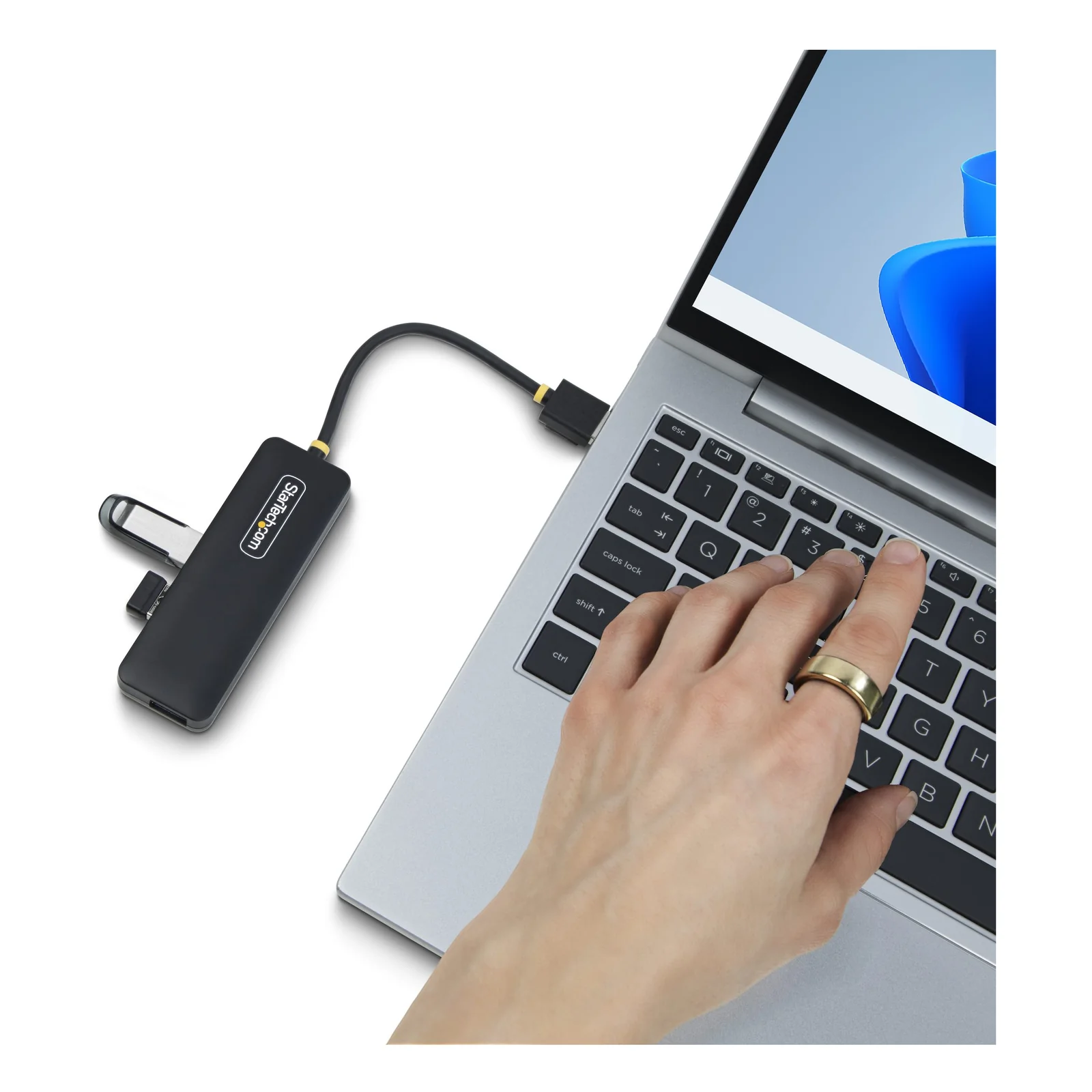 Main connectant le câble du hub USB-A à un ordinateur portable argenté, hub compact noir posé à gauche du clavier