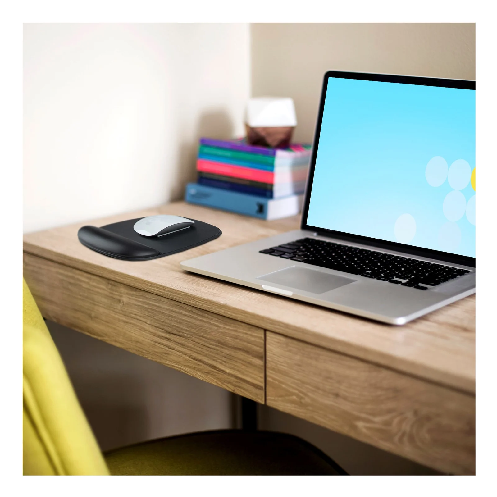 Tapis de souris noir avec repose-poignets posé sur un bureau en bois clair, souris blanche dessus et laptop ouvert à droite