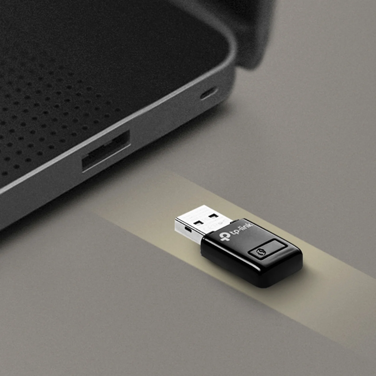 Adaptateur TL-WN823N présenté devant le port USB d'un appareil réseau sombre, sur le point d'être branché