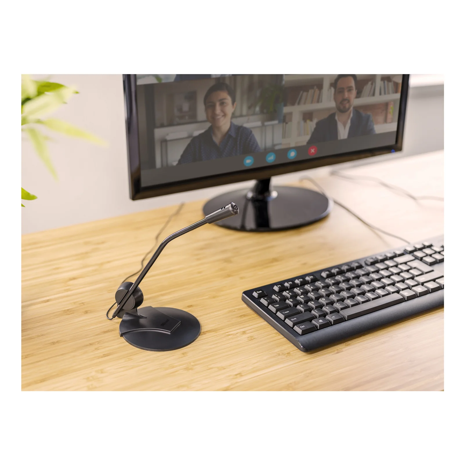 Microphone Trust 21674 posé sur un bureau avec clavier et écran affichant une visioconférence