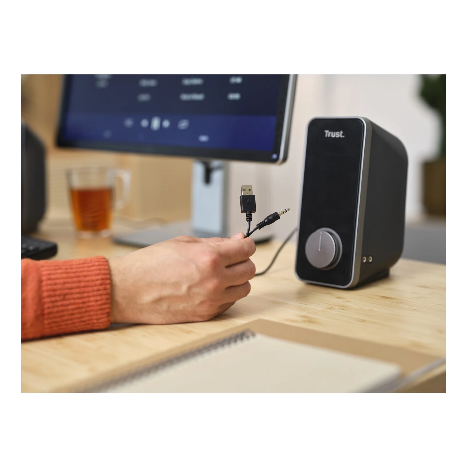Main branchant un câble USB sur une enceinte Trust Arys noire, vue rapprochée