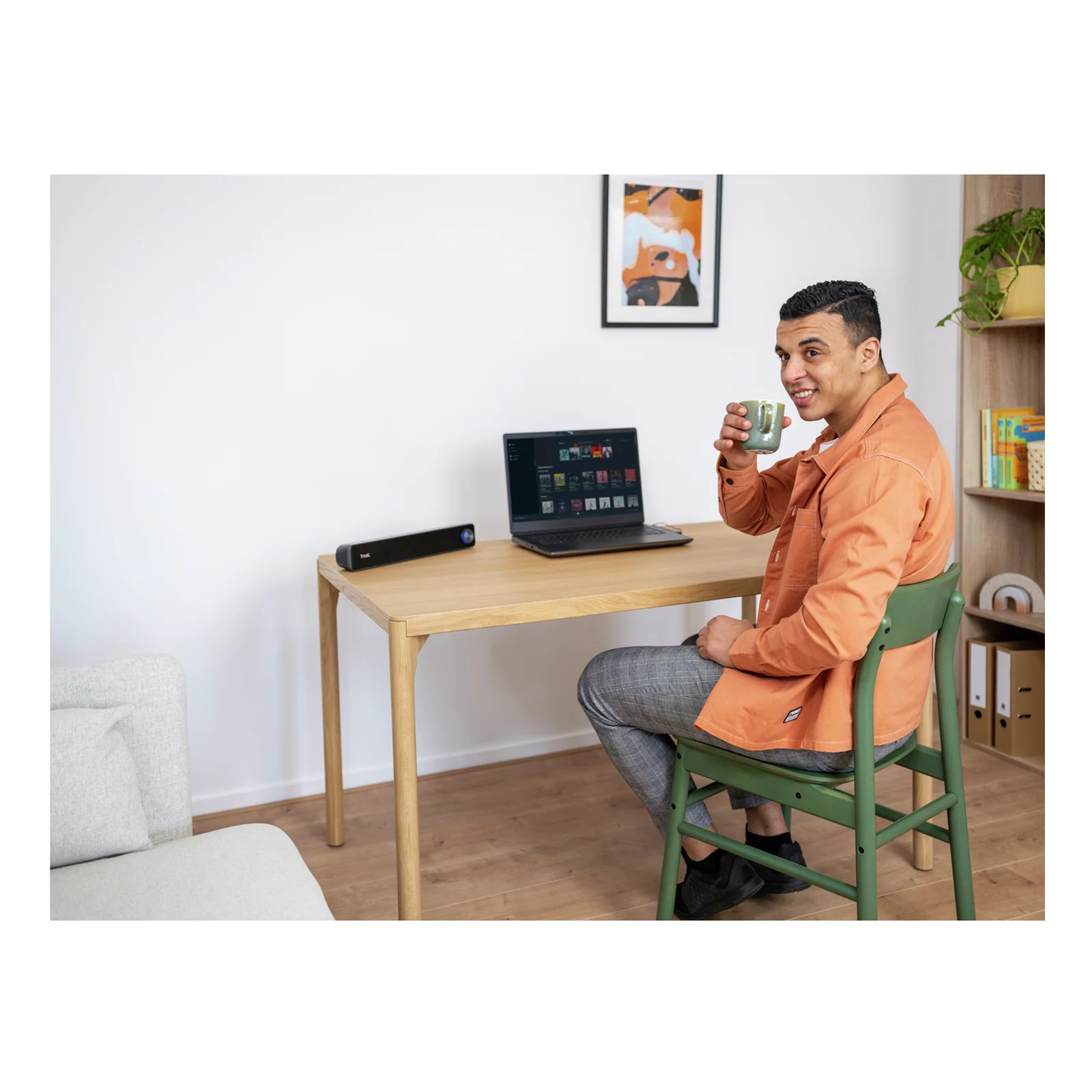 Homme en chemise orange assis à un bureau bois, soundbar posée devant un laptop