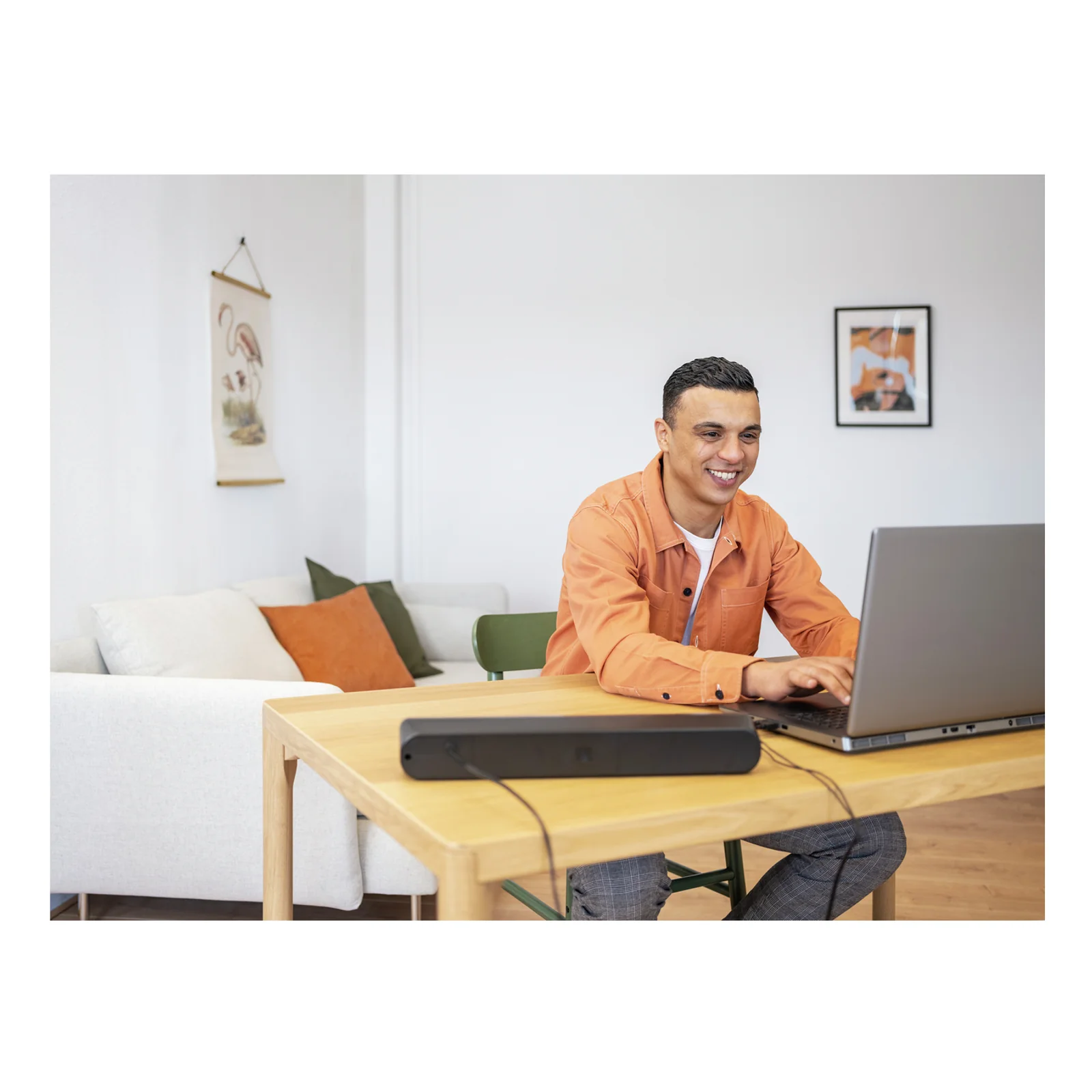 Homme assis sur canapé avec un laptop, soundbar noire posée sur la table
