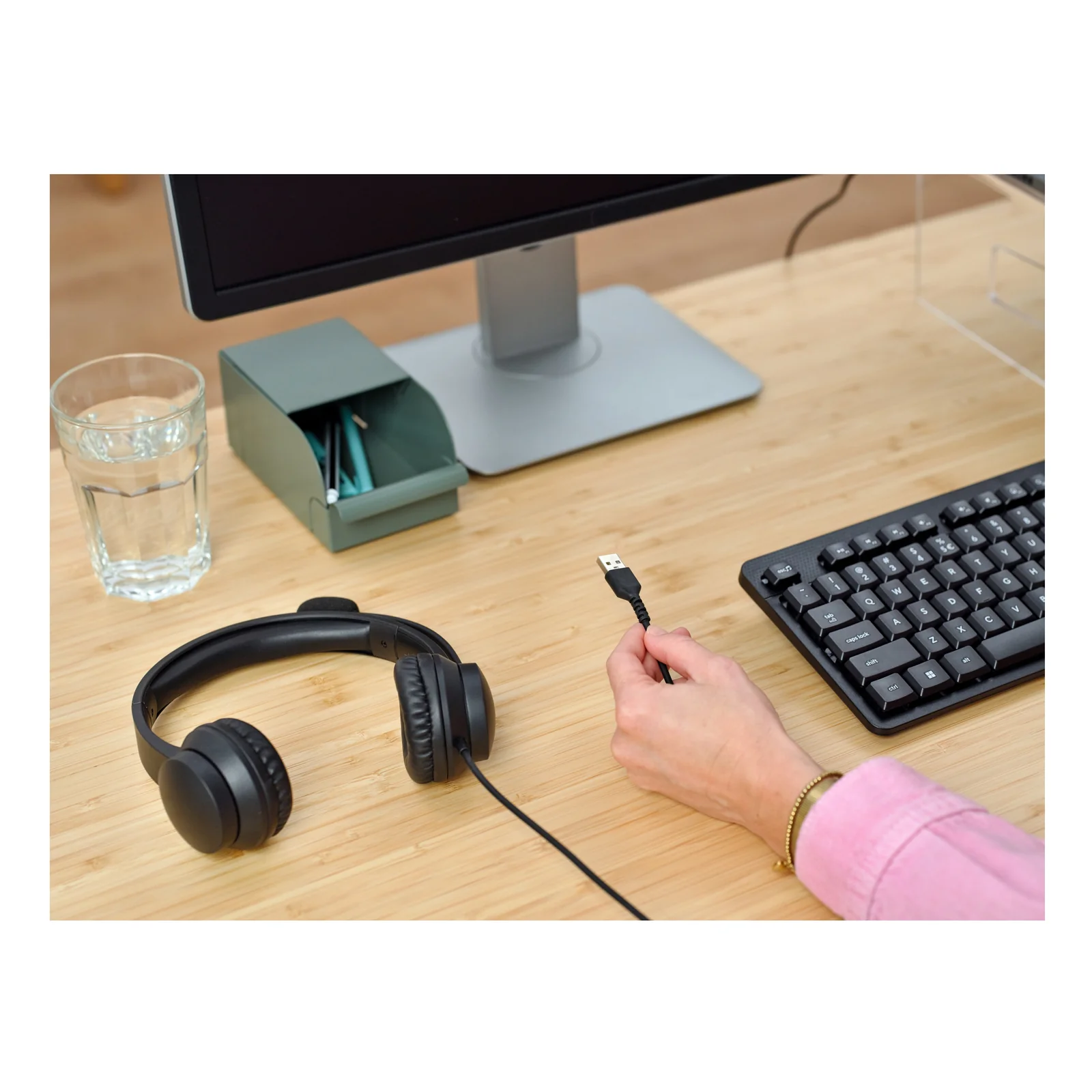 Casque Trust Ayda posé sur bureau, main tenant le câble USB pour branchement sur ordinateur portable
