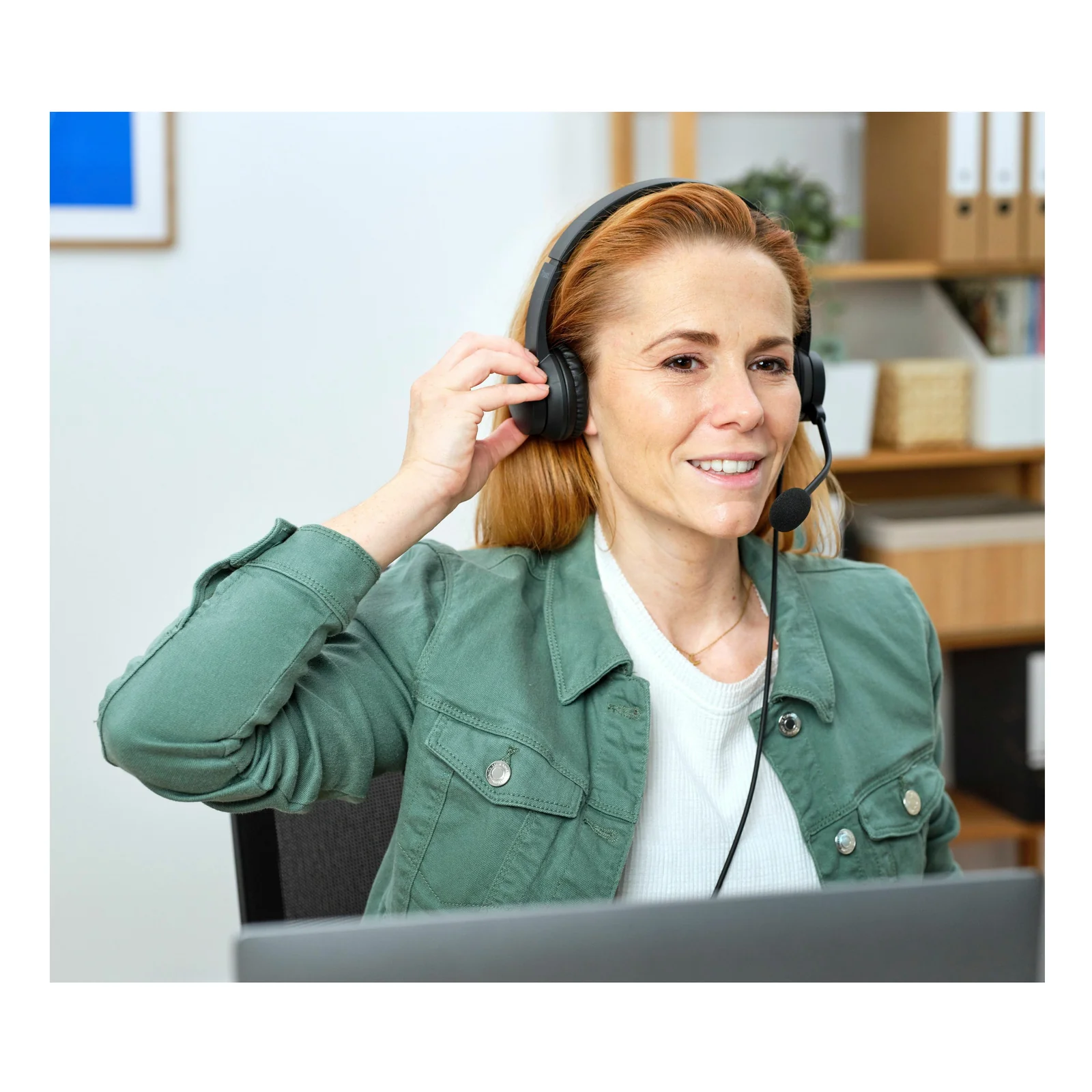 Femme rousse portant le casque Trust Ayda HS-150 noir à son bureau, souriant