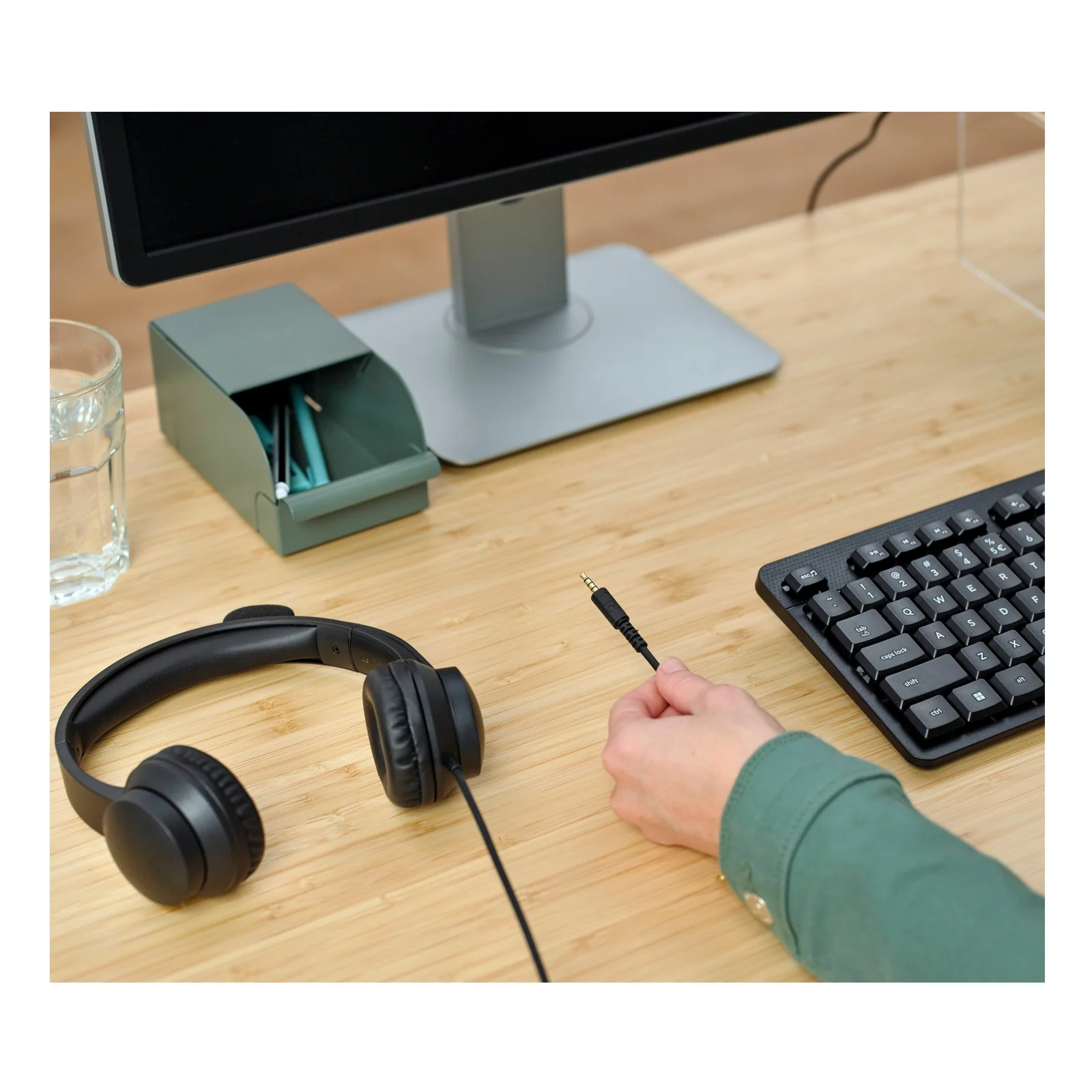 Casque Trust Ayda HS-150 posé sur un bureau à côté d'un clavier, main tenant un stylo
