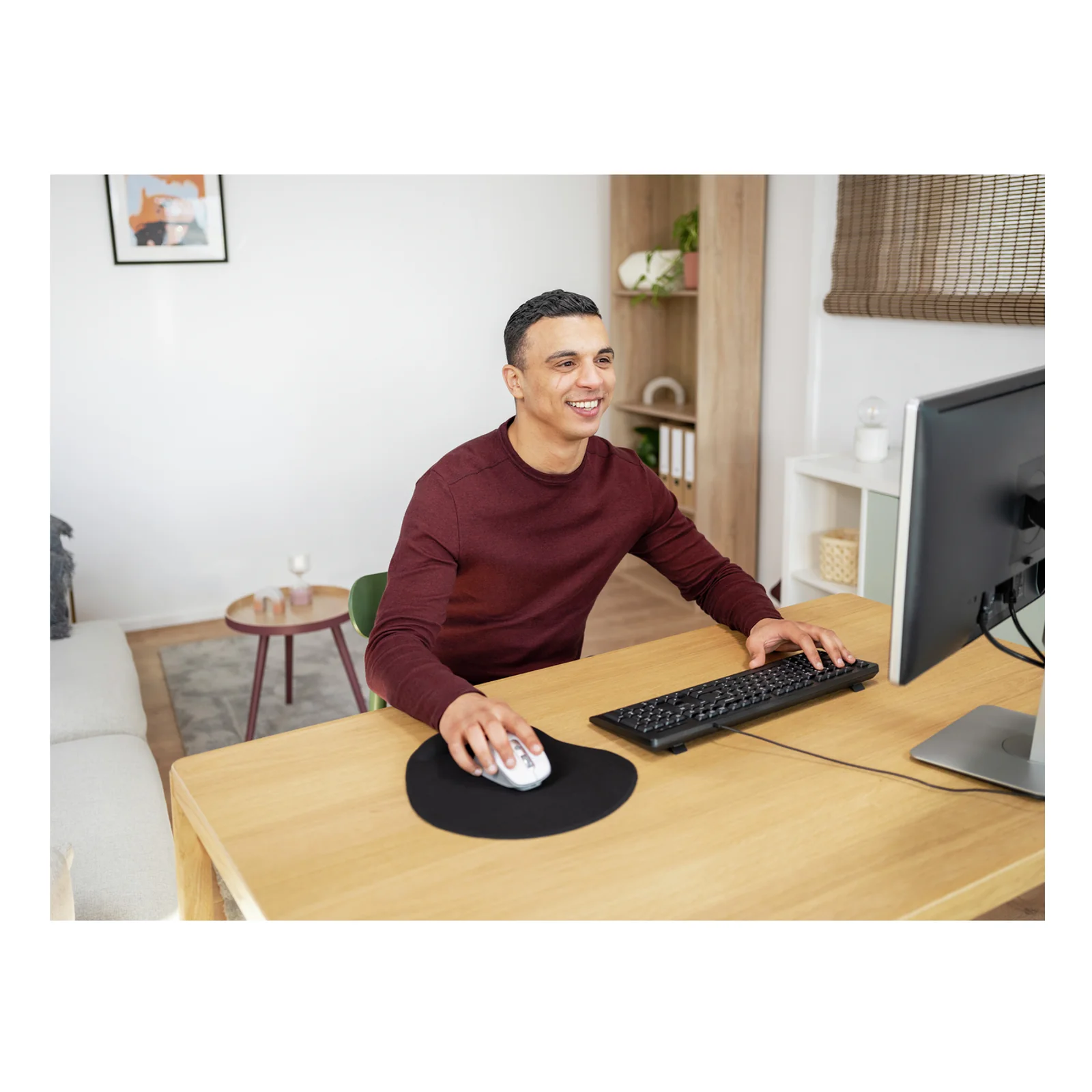 Homme en pull bordeaux au bureau, tapis noir sous la souris, moniteur et clavier visibles