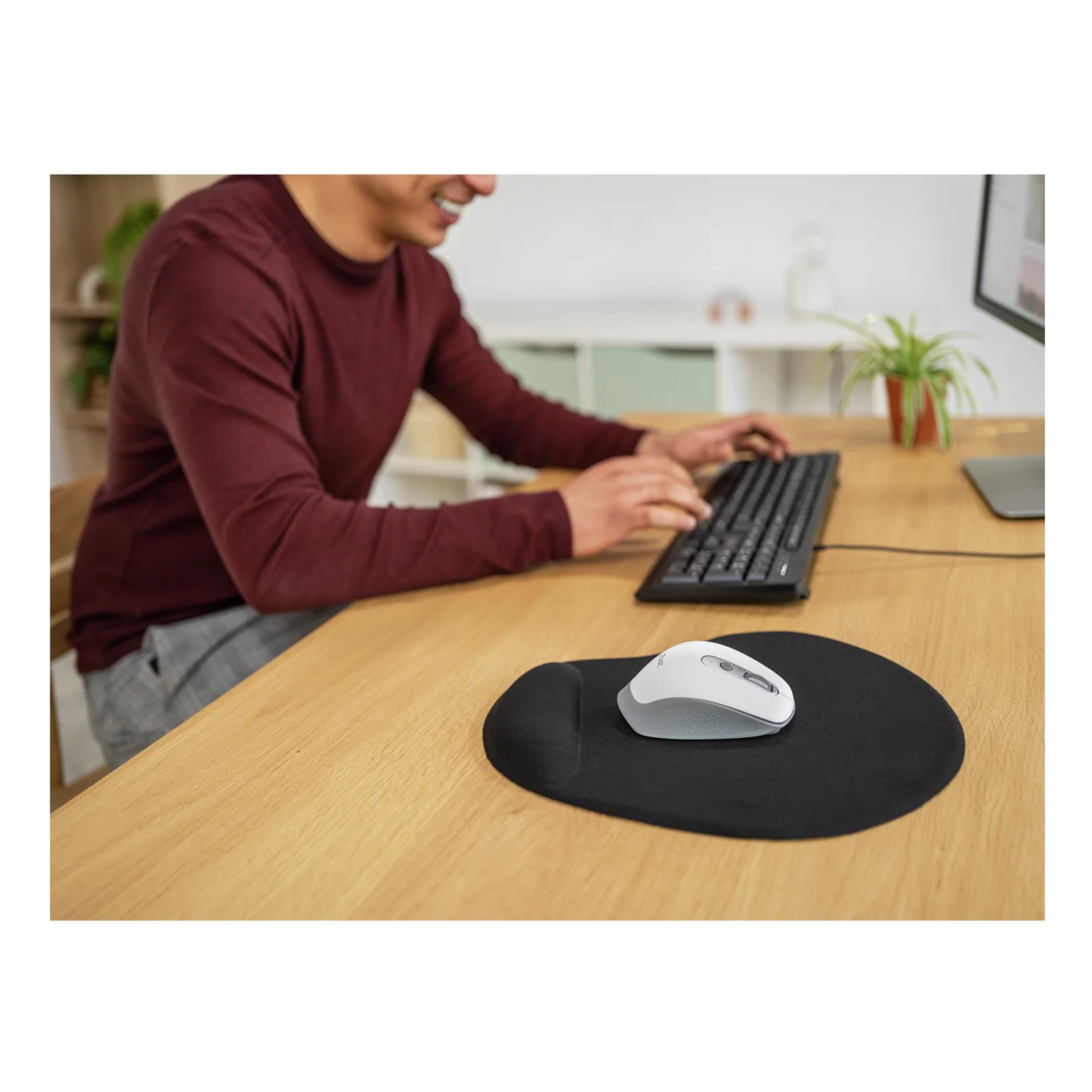 Personne avec souris argentée sur tapis ovale noir, clavier et bureau bois visibles