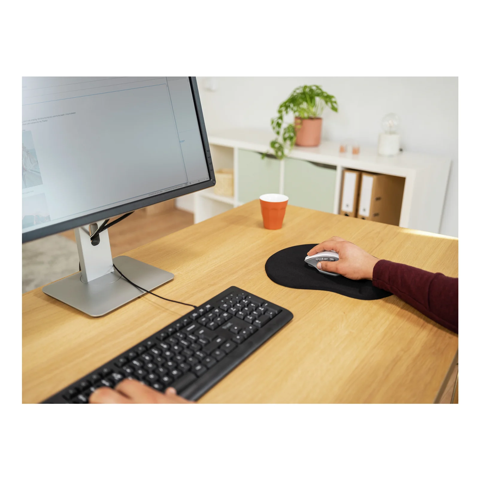 Main sur souris, tapis noir sur bureau blanc, clavier, écran de bureau et tasse en fond