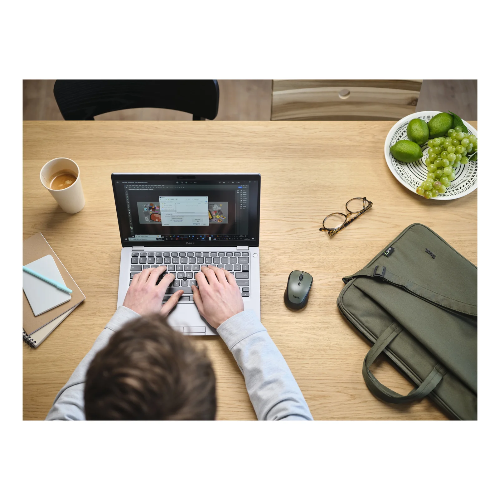 Vue aérienne lifestyle, personne travaillant sur laptop, mallette Trust Bologna verte posée sur table