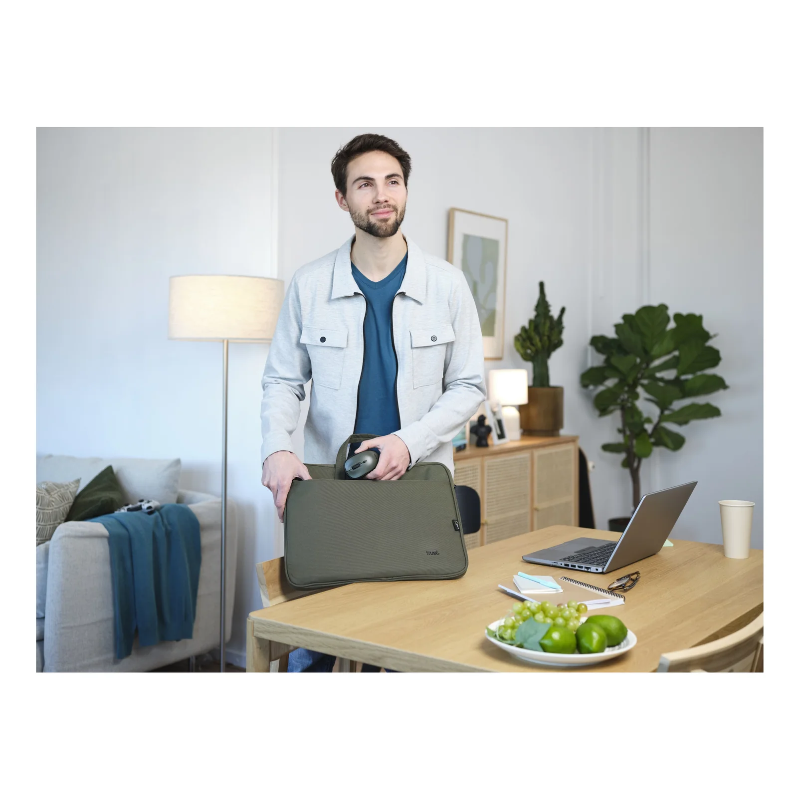 Photo lifestyle, homme debout tenant la mallette Trust Bologna verte près d'une table de travail