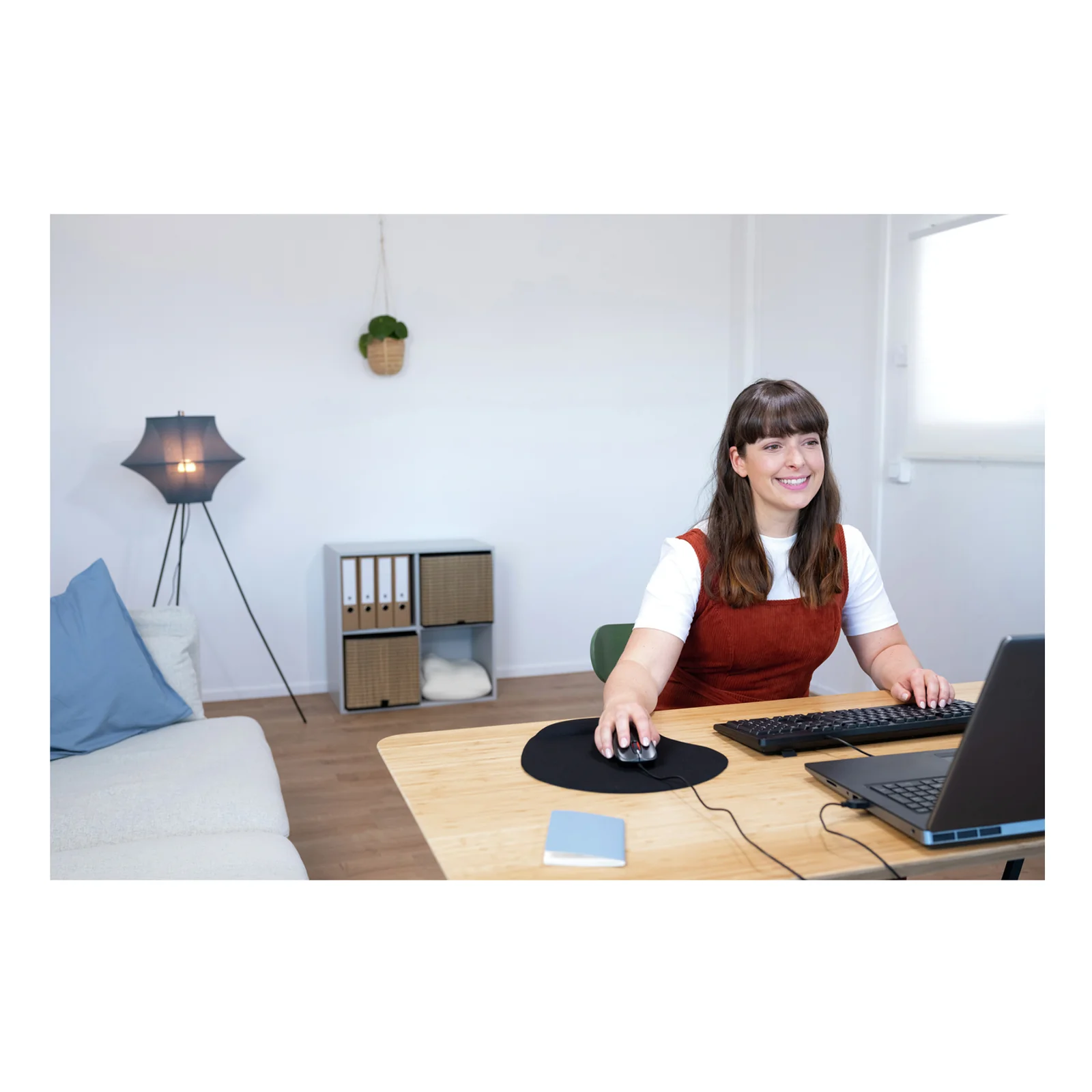 Femme utilisant une souris Trust Carve noire sur un bureau avec ordinateur portable