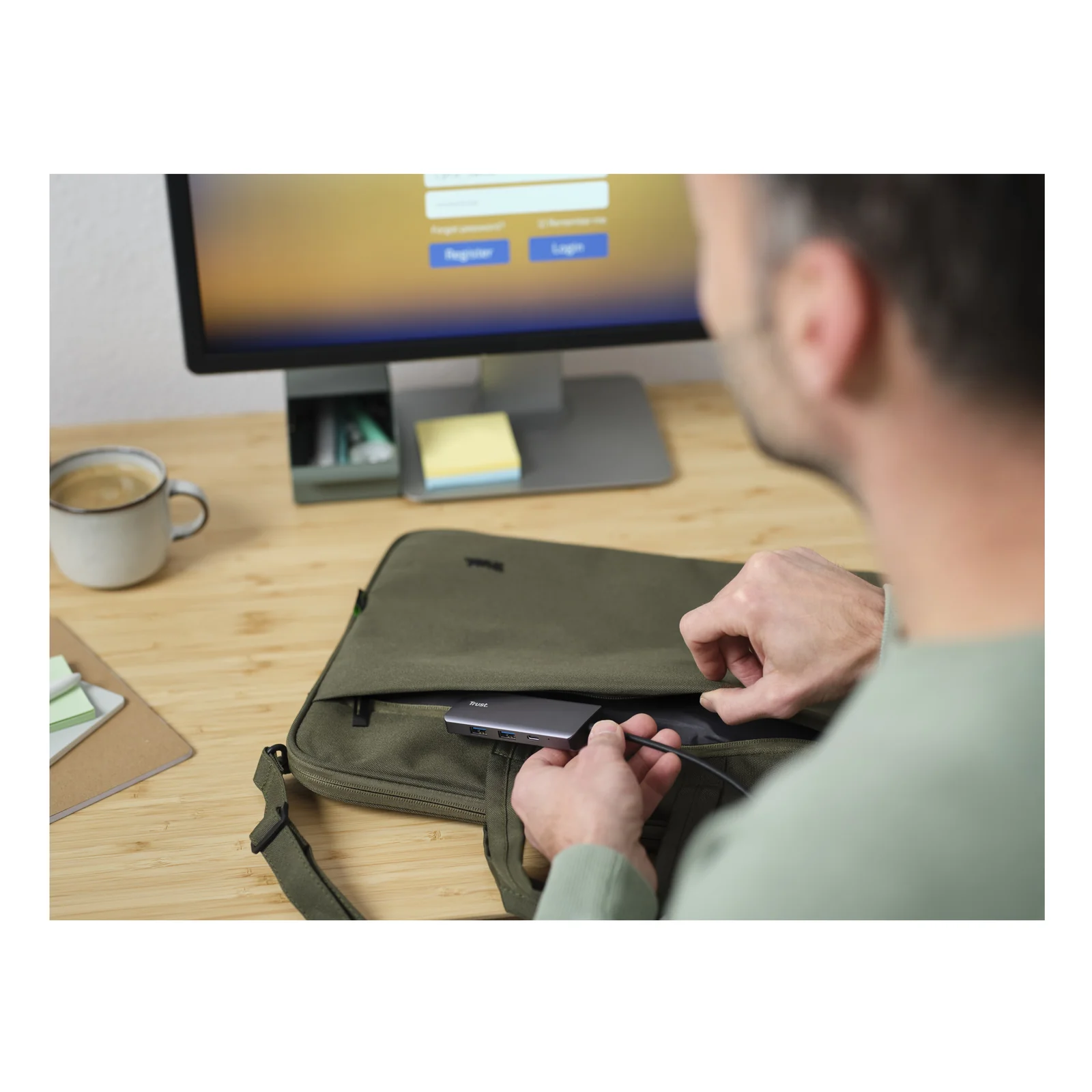 Personne devant un écran de bureau, tenant une pochette pour ordinateur, hub Trust Dalyx en contexte usage