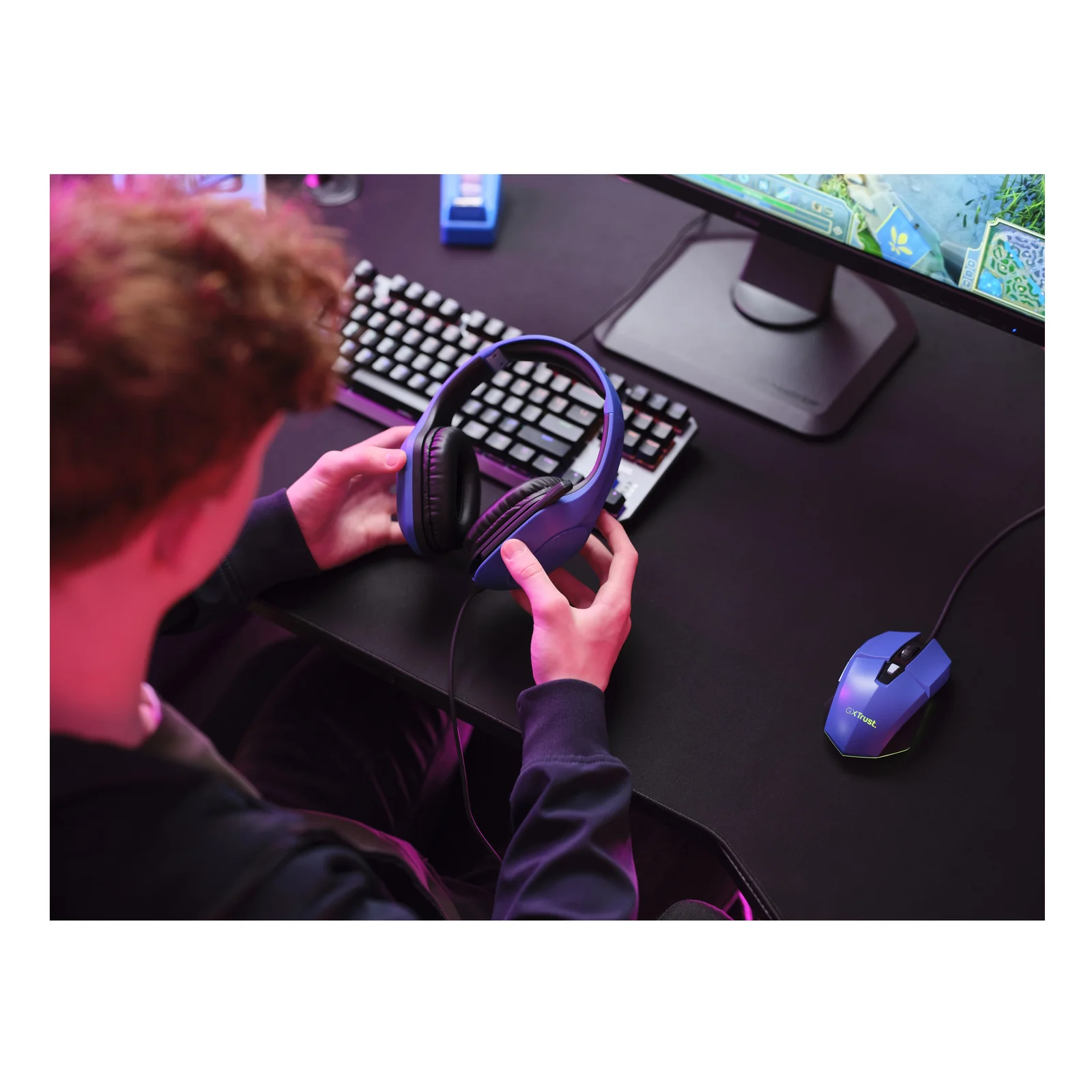 Utilisateur portant le casque Trust GXT 415B Zirox bleu à un bureau gaming avec clavier et souris