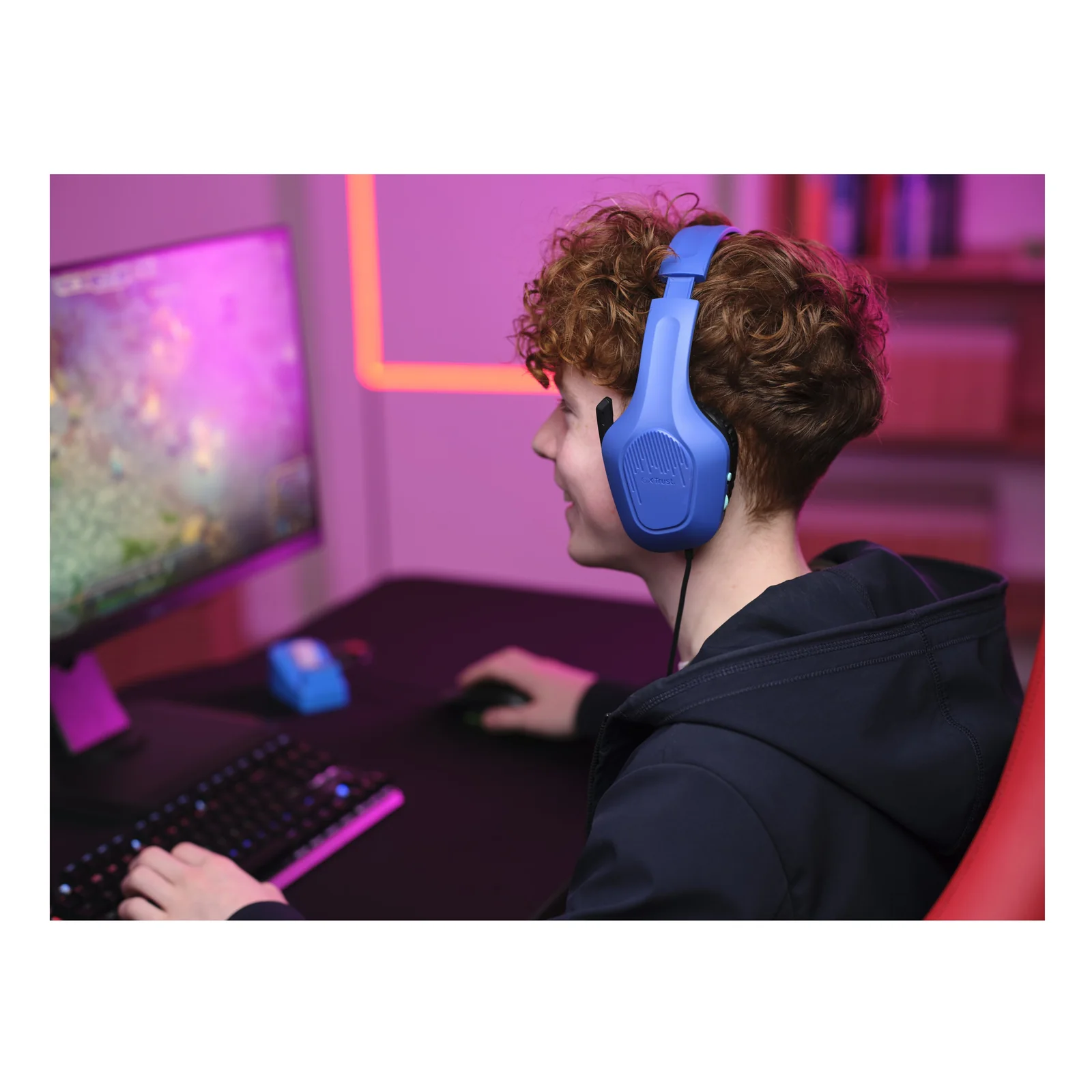 Joueur portant le casque Trust GXT 415B Zirox bleu devant un écran de jeu, éclairage ambiant rose