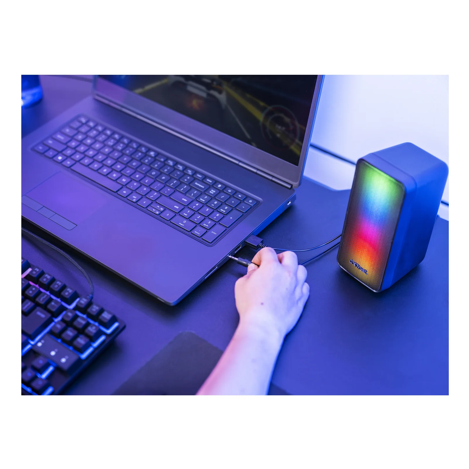 Main branchant le câble USB sur une enceinte Trust GXT 611 Wezz posée sur un bureau