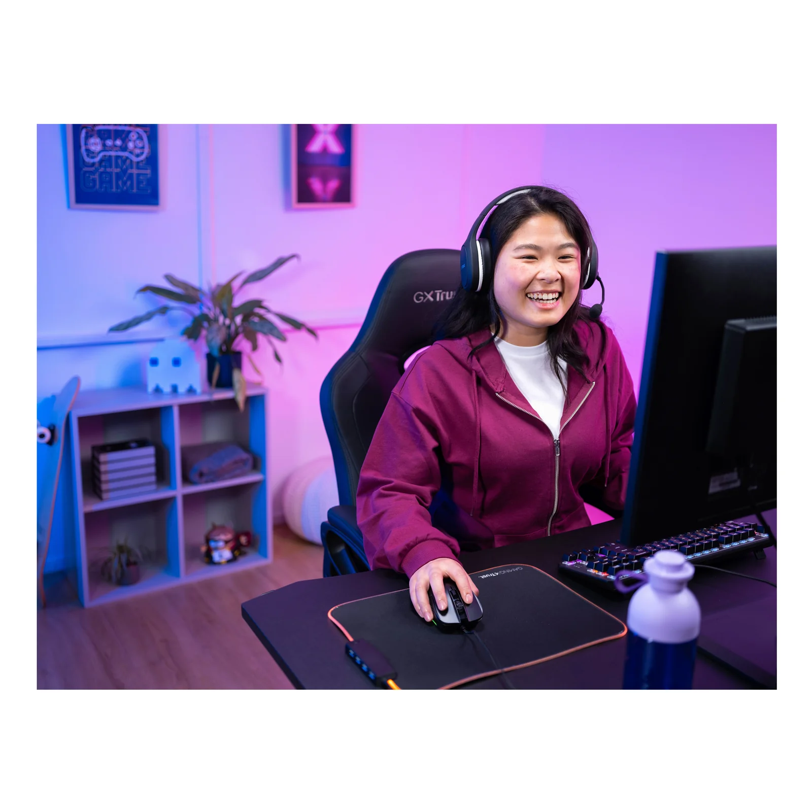 Jeune femme souriante avec casque gaming à son bureau, setup gaming éclairé en violet et bleu