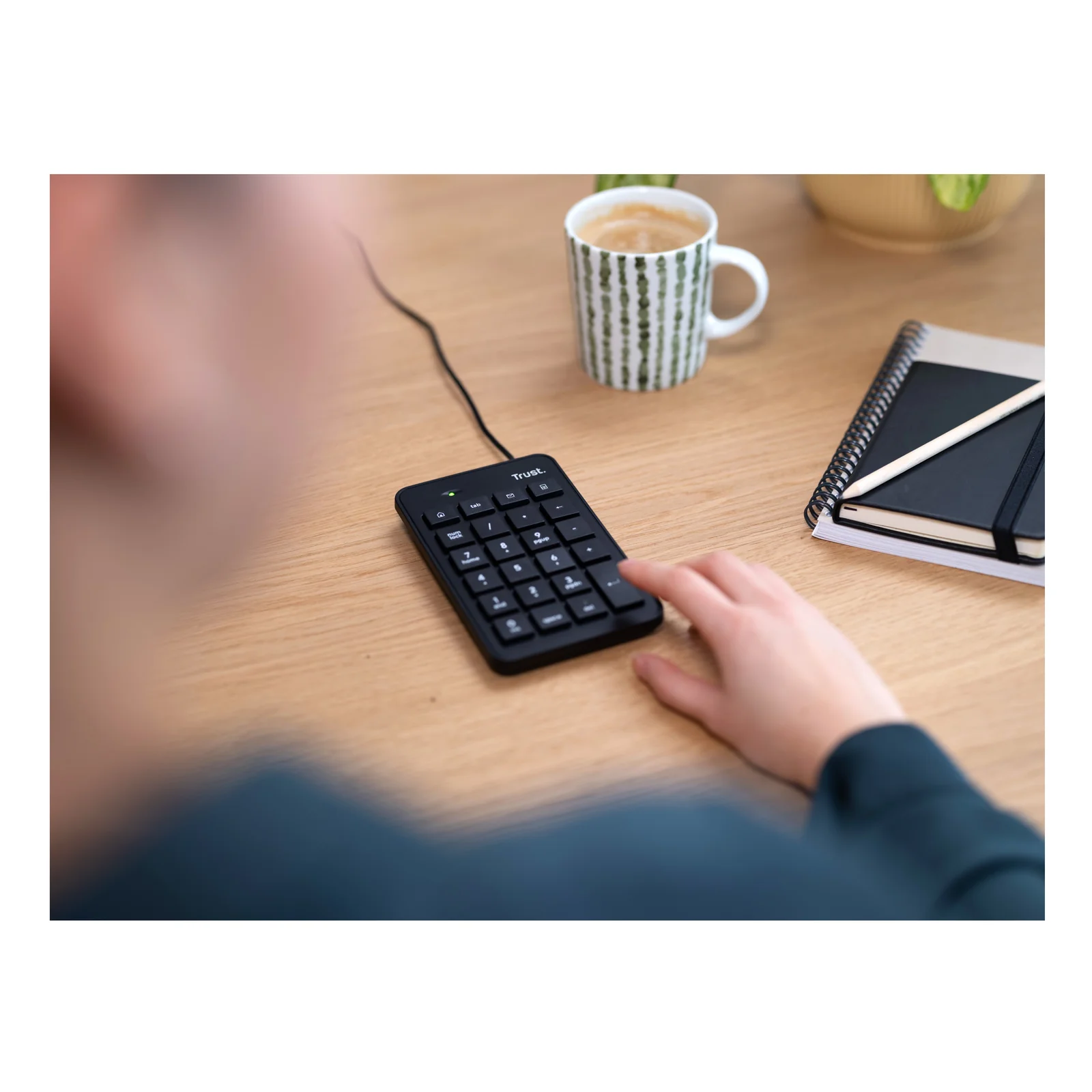 Photo d'usage, personne utilisant le pavé numérique Trust sur bureau en bois avec tasse