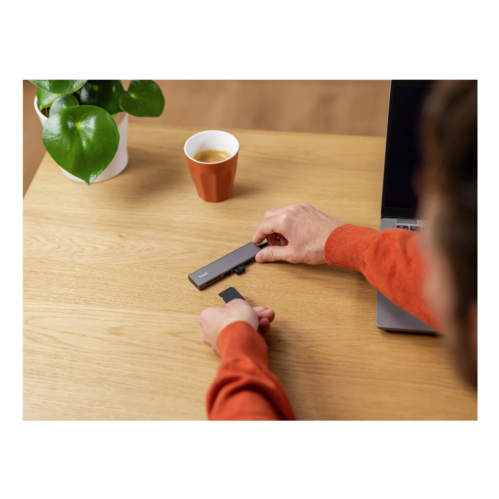 Hub Trust Halyx branché sur un laptop posé sur un bureau en bois, utilisateur en pull orange