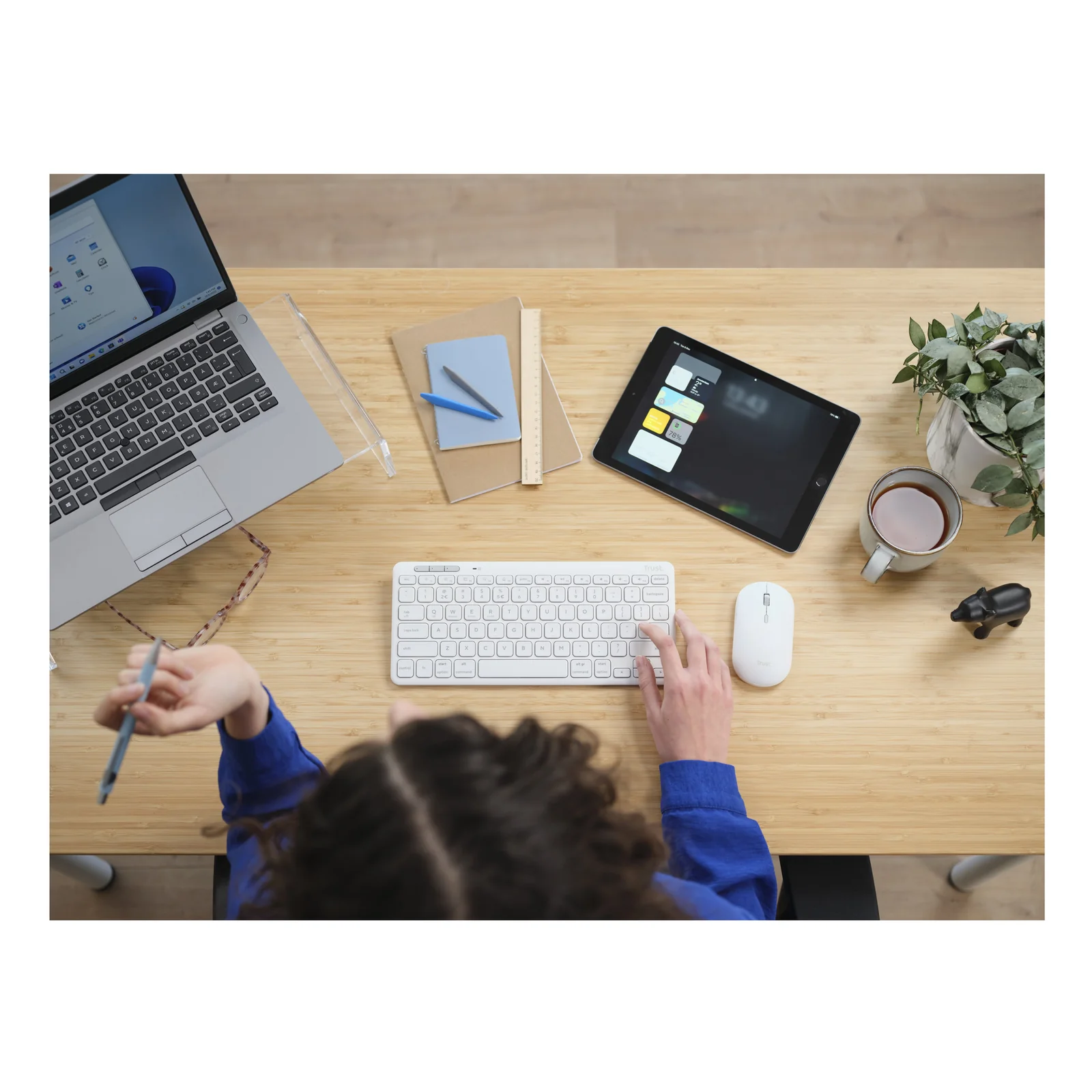Personne utilisant le combo Trust Lyra sur un bureau en bois avec tablette et ordinateur portable