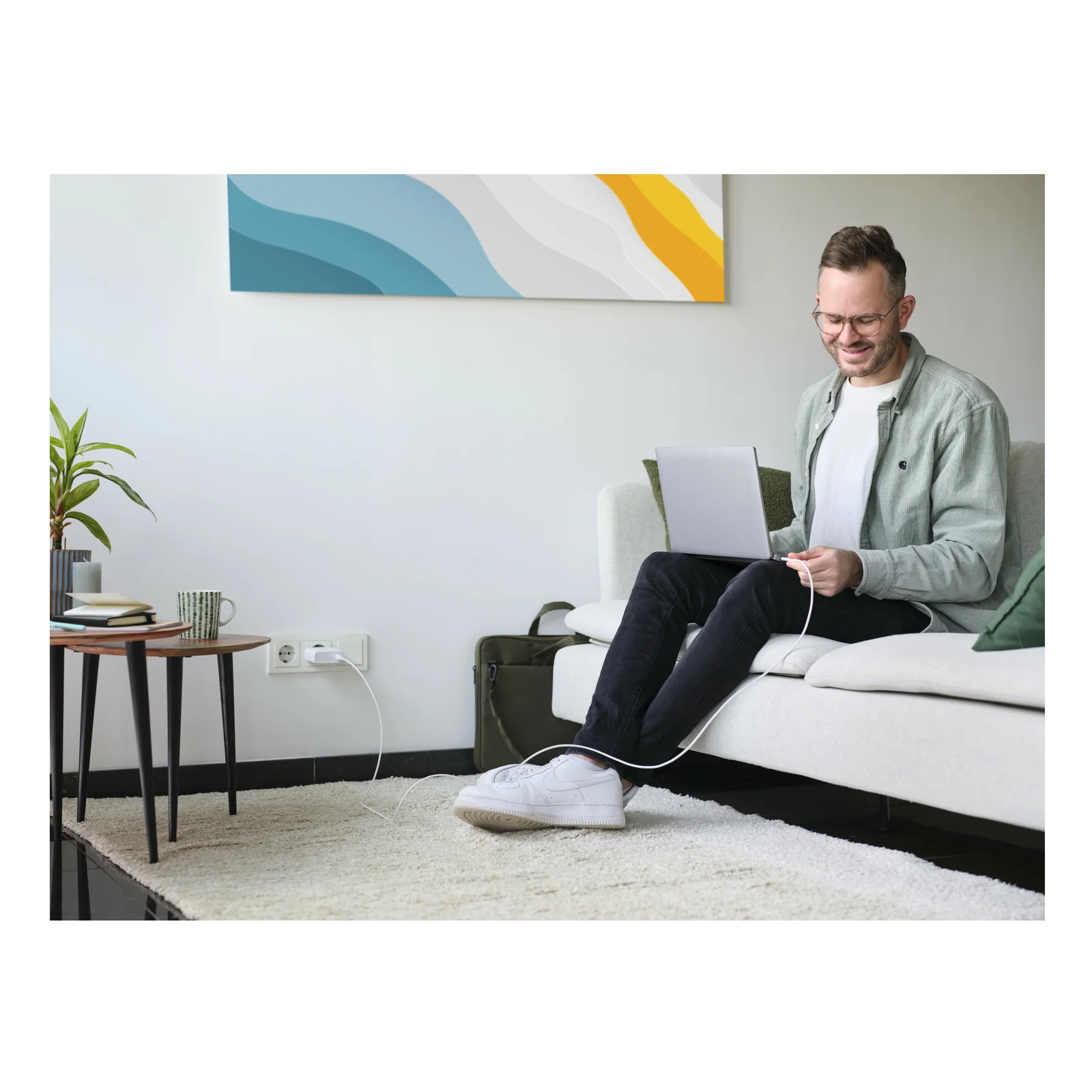 Photo d'ambiance, homme assis sur un lit, ordinateur portable relié au chargeur Trust Maxo