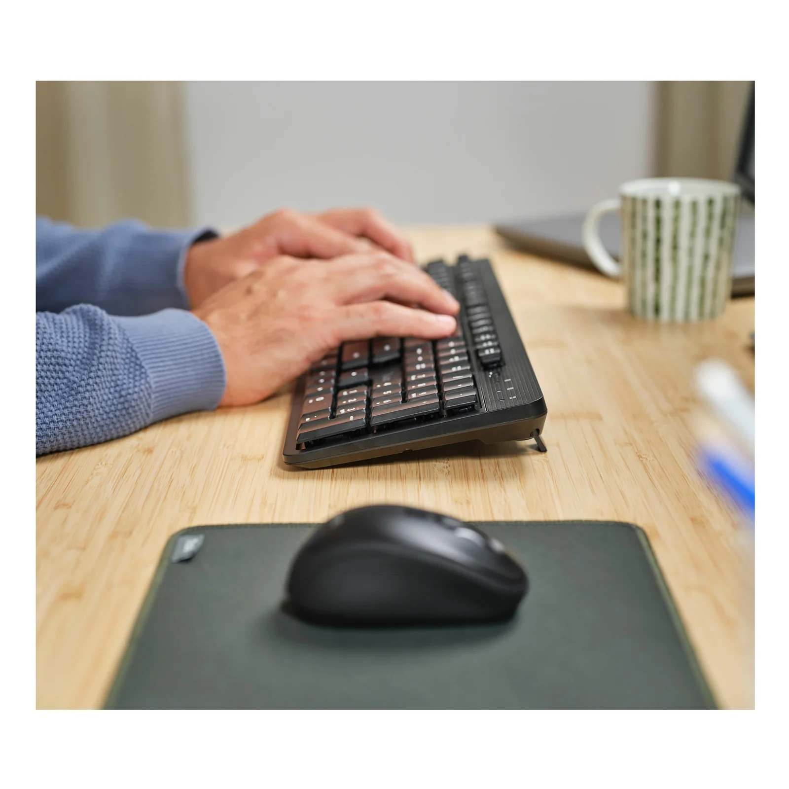 Mains posées sur le clavier Trust Ody II noir, souris à droite sur bureau en bois
