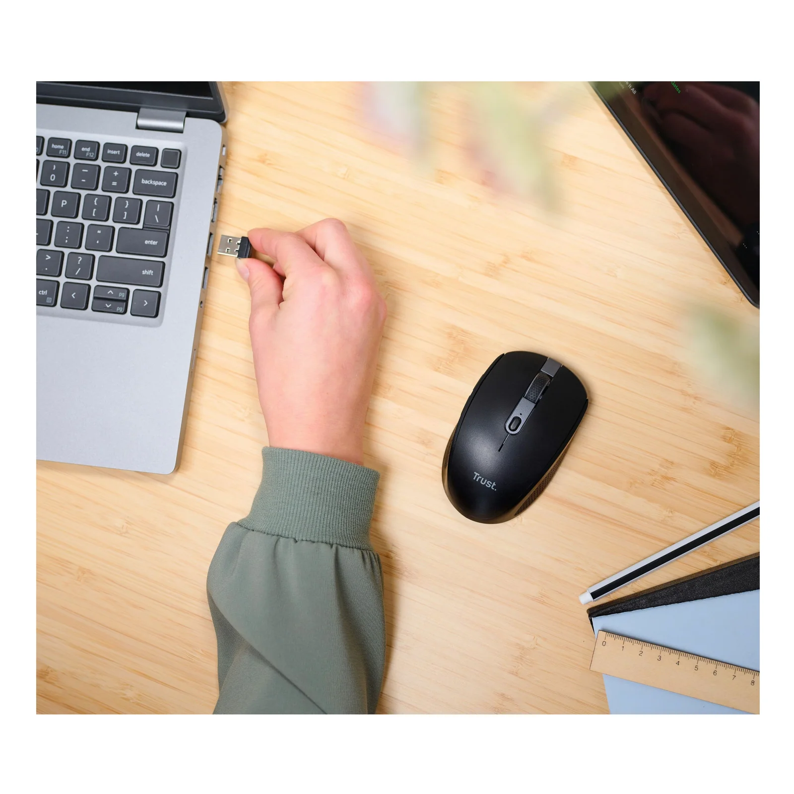 Main insérant un nano-récepteur USB dans le port d'un laptop, souris Trust Ozaa visible au fond