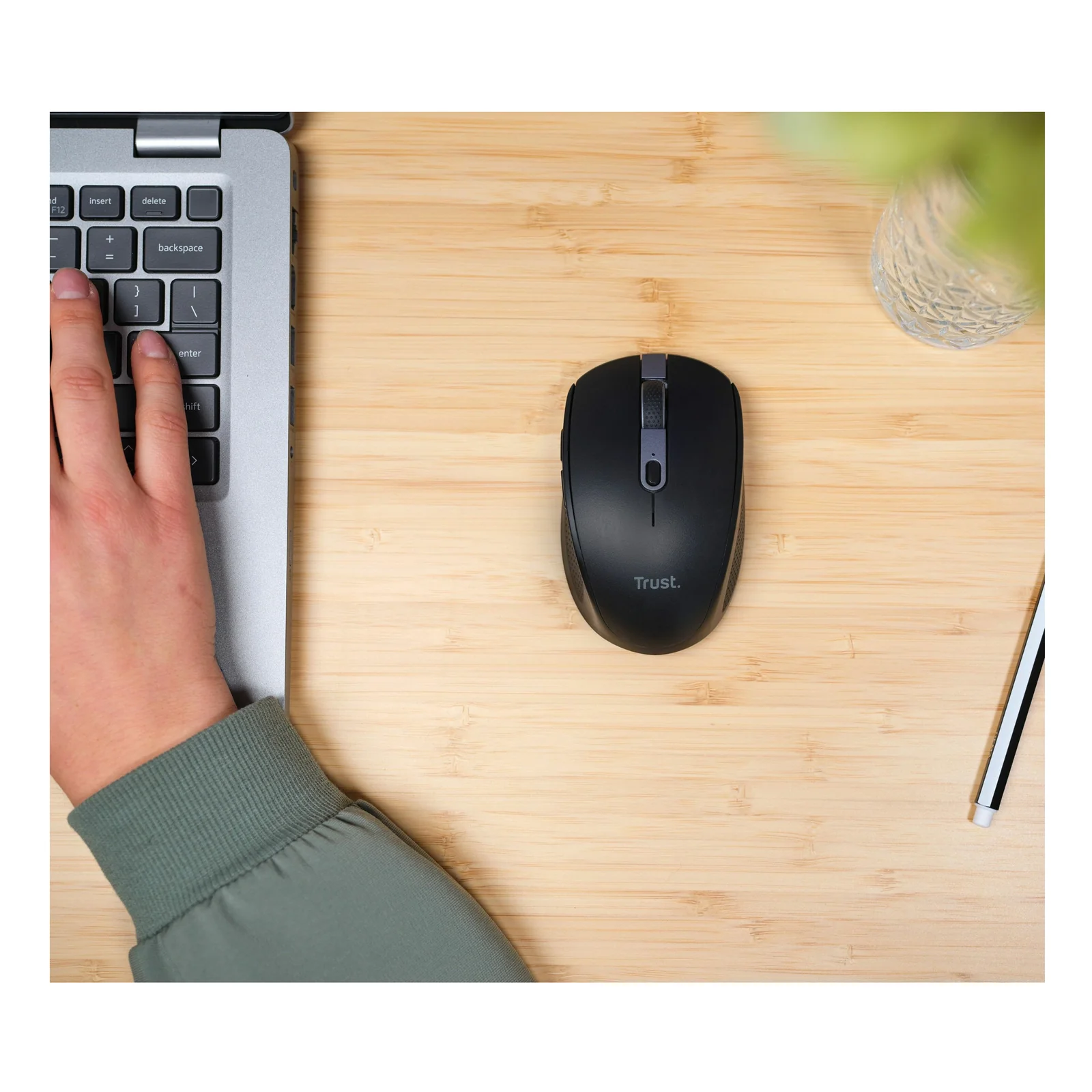 Main posée sur la souris Trust Ozaa noire, bureau en bois avec carnet et stylo