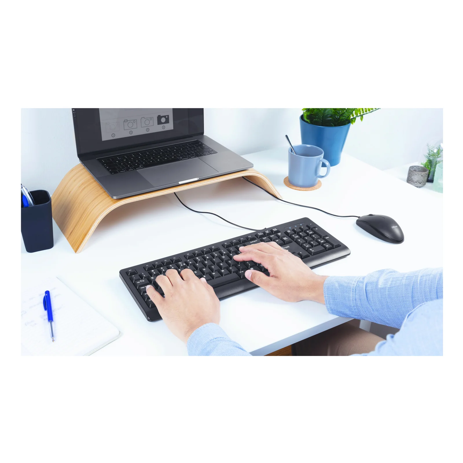 Clavier Trust Primo noir utilisé sur un bureau en bois avec support laptop, vue en angle