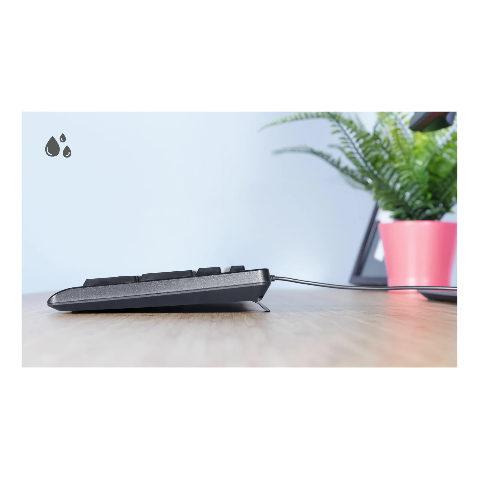 Vue arrière trois quarts, clavier Trust Primo noir sur bureau, pictogramme résistance aux éclaboussures