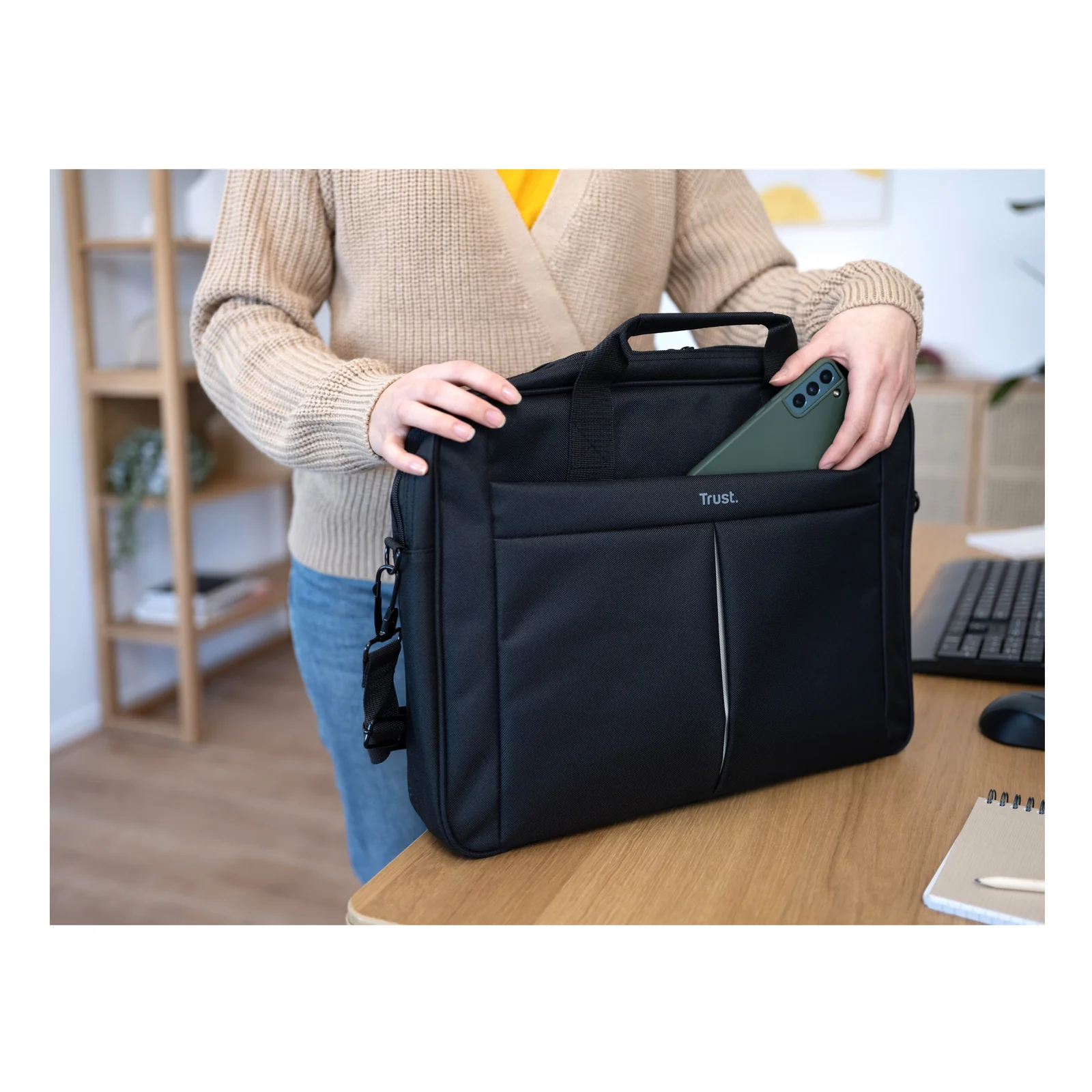 Mains tenant la sacoche Trust Primo et accédant à la poche avant, plan rapproché sur un bureau
