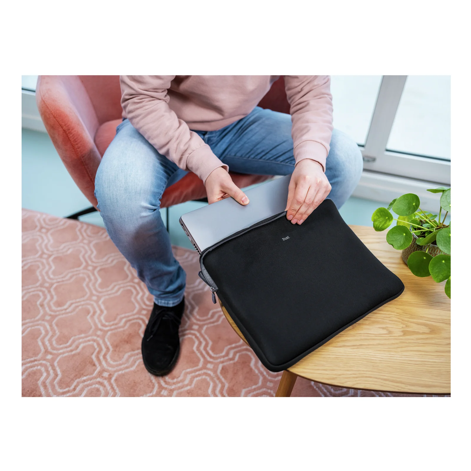 Homme en jeans clairs tenant un laptop protégé par la housse Trust noire, en intérieur