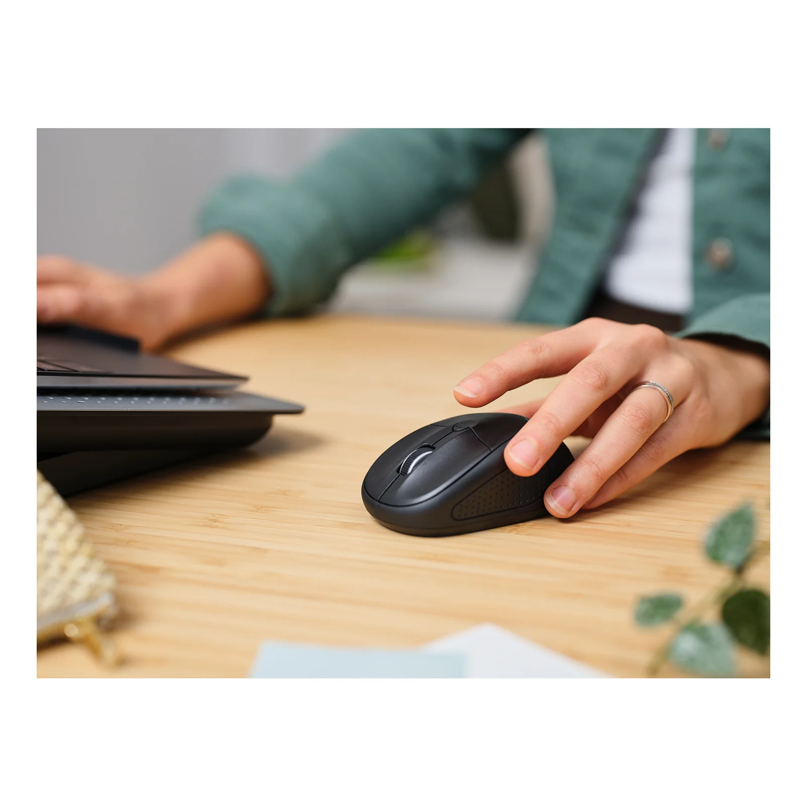 Main posée sur la souris Trust Primo noire sur un bureau en bois