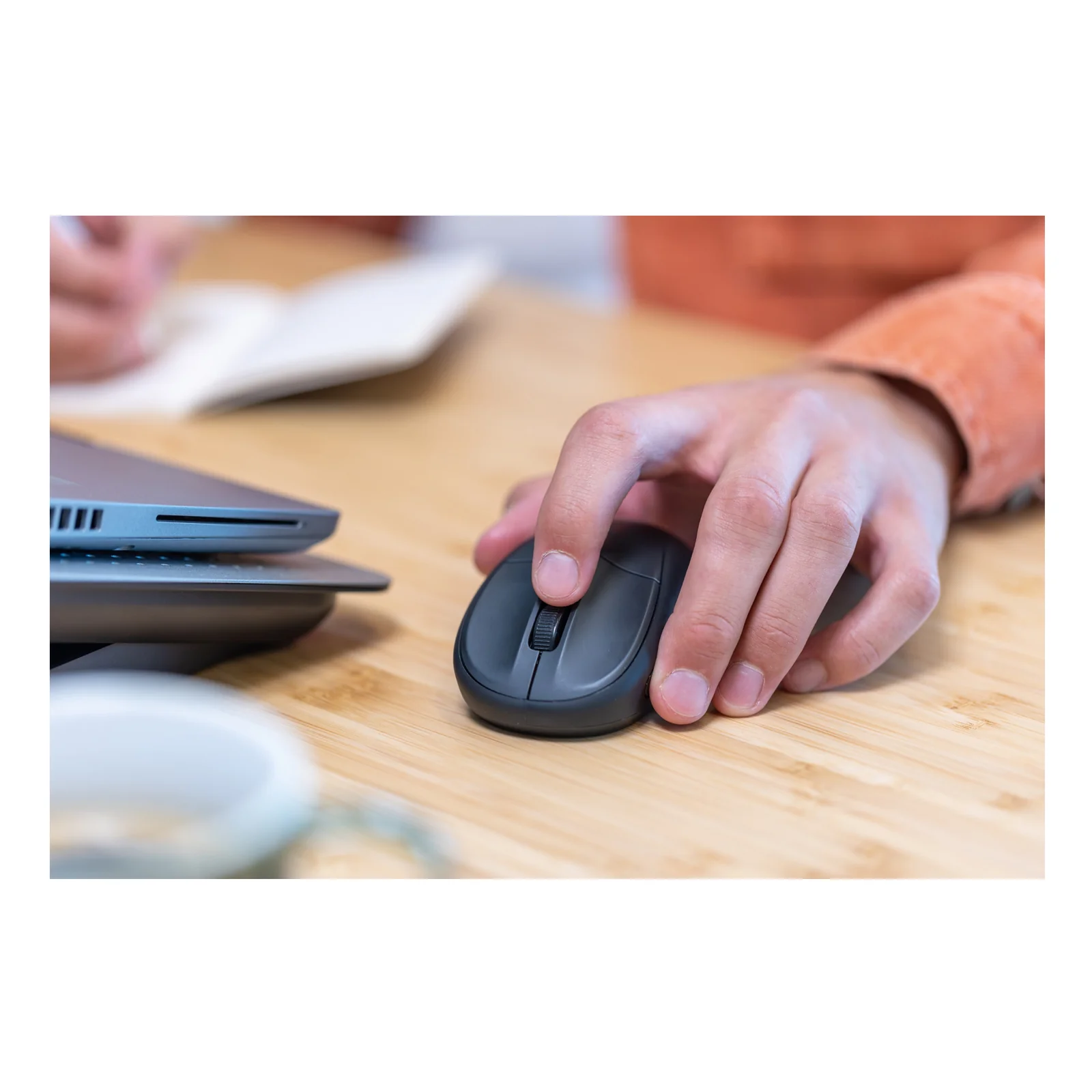 Main utilisant une souris foncée sur bureau en bois, ordinateur portable à côté
