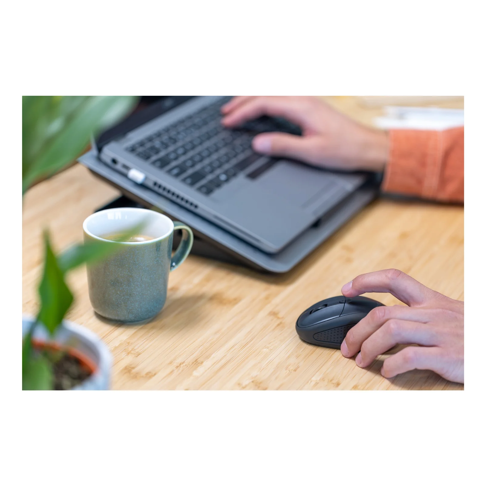 Personne utilisant une souris sans fil foncée sur bureau en bois, laptop ouvert