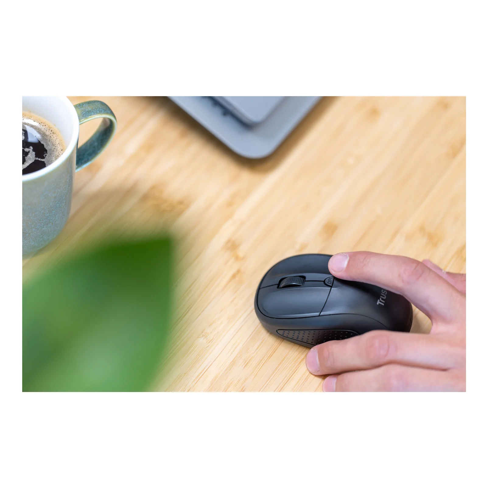 Main posée sur une souris sans fil foncée, tasse de café sur bureau en bois